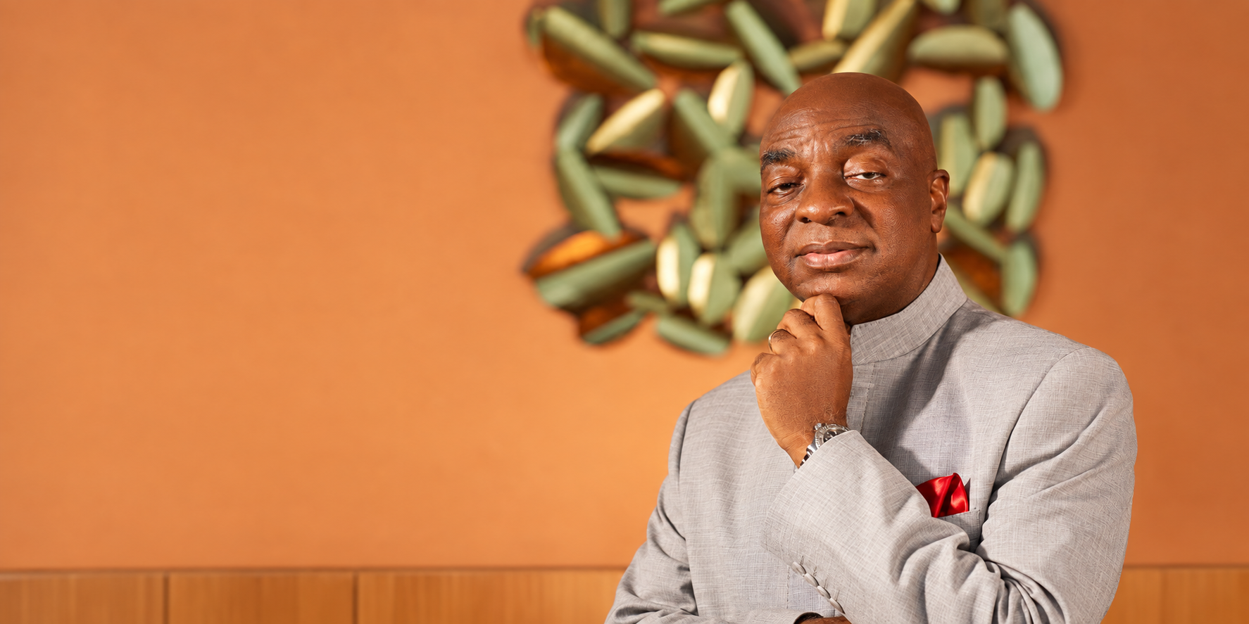 Bishop David Oyedepo in a grey suit, resting his chin on his hand